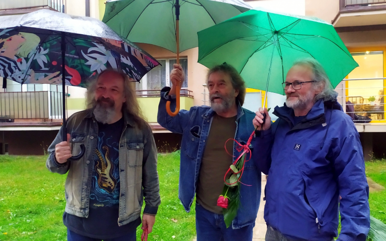 Trzech mężczyzn trzyma w ręku otwarte nad głowami parasolki