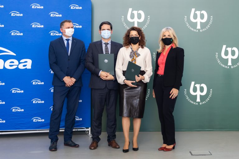 Obok siebie stoją cztery osoby , dwie z nich trzymają zielone teczki