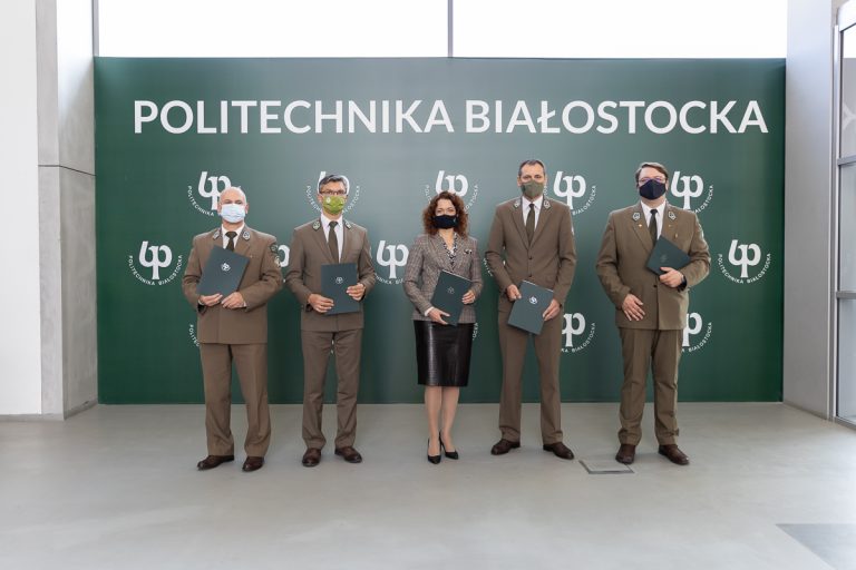 Czterech mężczyzn i kobieta stoją trzymając w dłoniach teczki z umową