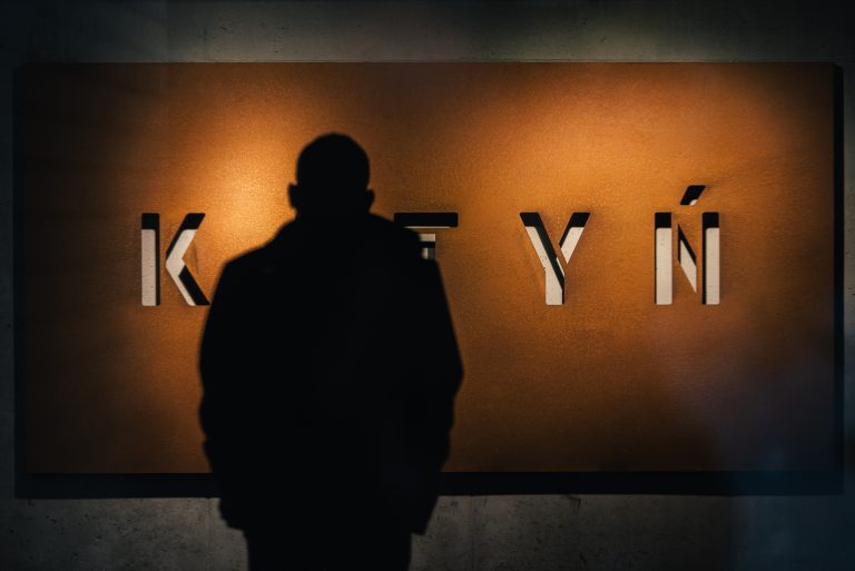 Mężczyzna stoi przed ścianą z napisem KATYŃ
