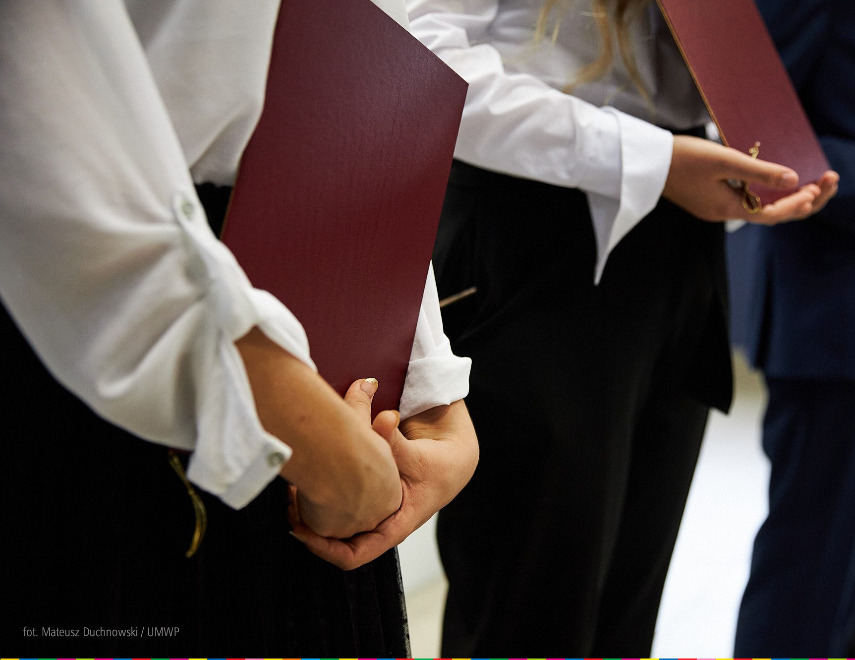 Kilka osób stoi w rzędzie, w rękach trzyma bordowe teczki