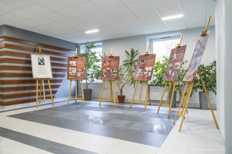 W korytarzu stoją sztalugi wypełnione fotosami