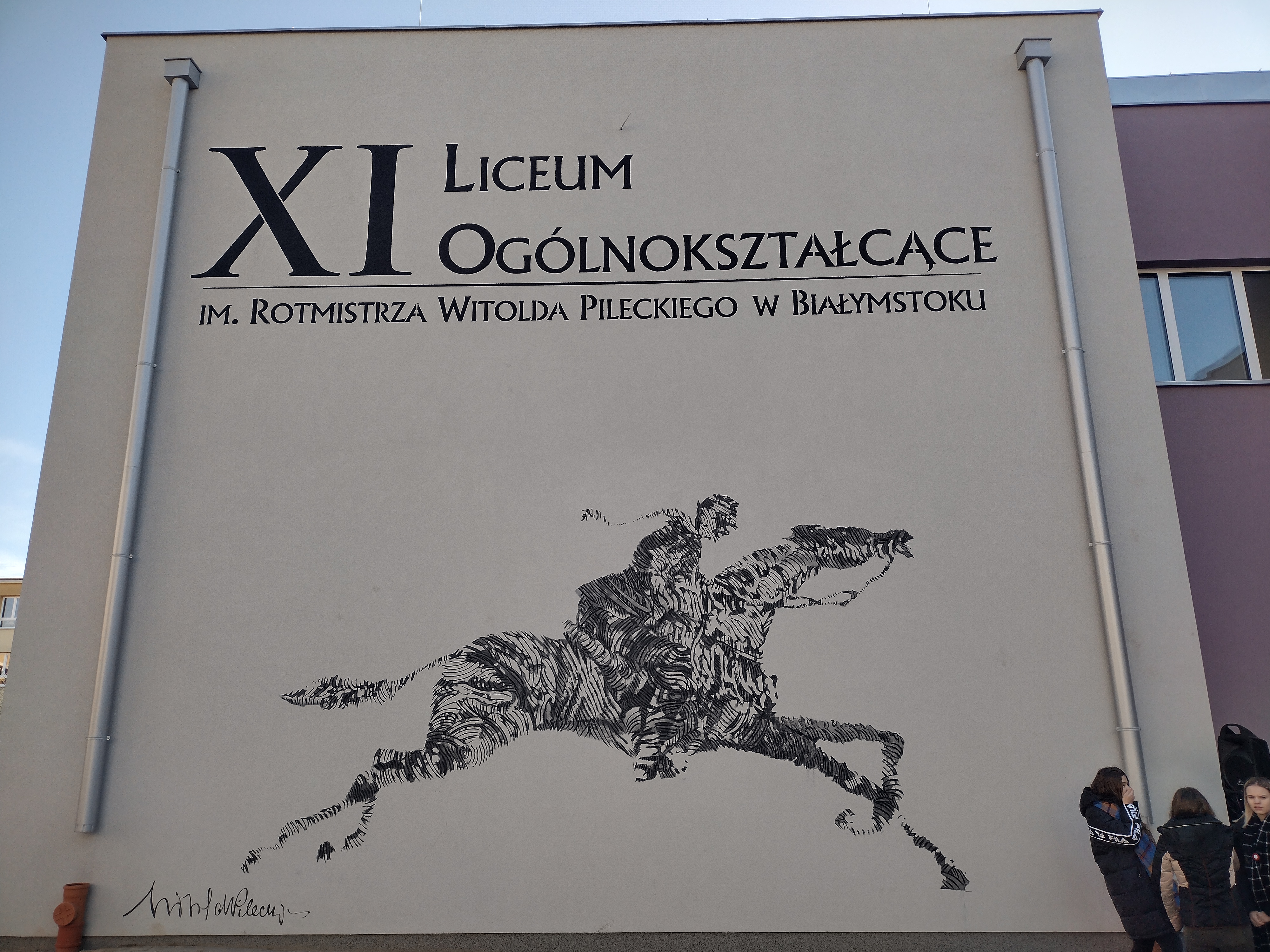 Mural na ścianie ukazujący symbolicznego rotmistrza Witolda Pileckiego jadącego na koniu. Nad postacią jadącą na koniu znajduje się napis: XI Liceum Ogólnokształcące im. rotmistrz Witolda Pileckiego w Białymstoku