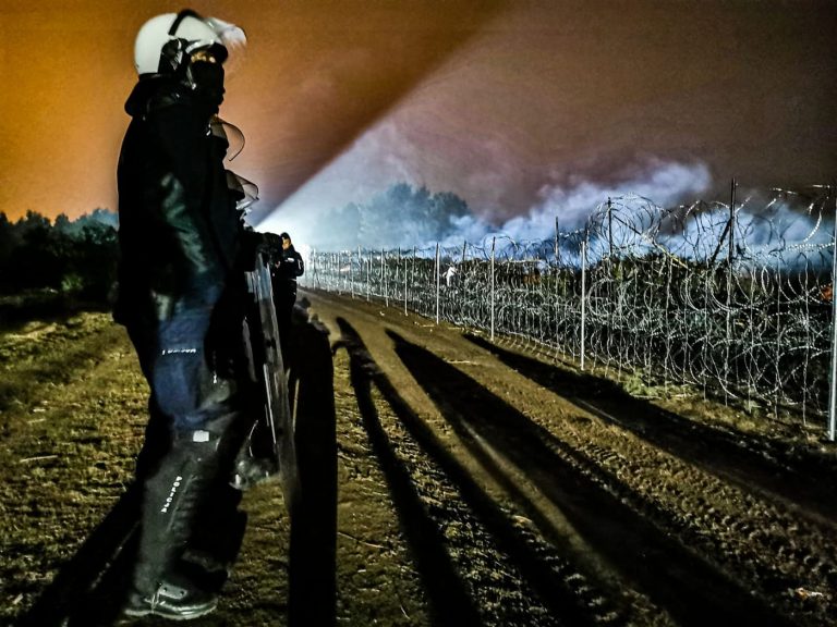 Jest noc, którą rozświetla z oddali reflektor samochodowy . Z lewej strony stoi szwadron uzbrojonych policjantów, choć na zdjęciu widać jednego, który stoi bokiem. Funkcjonariusze stoją na przeciw płotu z drutu kolczastego
