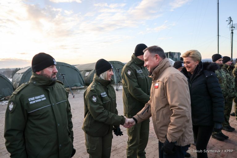 Z strażnikami granicznymi, którzy stoją w rzędzie wita się para prezydencka, Z przodu idzie mężczyzna w beżowej kurtce (prezydent Polski) i podaje dłoń funkcjonariuszce. Za prezydentem idzie jego żona w ciemnej kurtce, i podaje dłoń funkcjonariuszowi