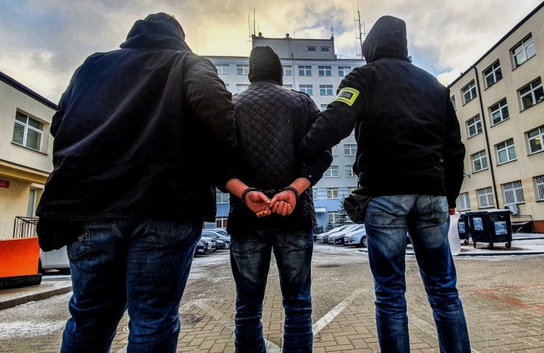 Dwaj policjanci trzymają skutego kajdankami mężczyznę