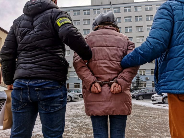 Dwaj policjanci trzymają skutą kajdankami kobietę