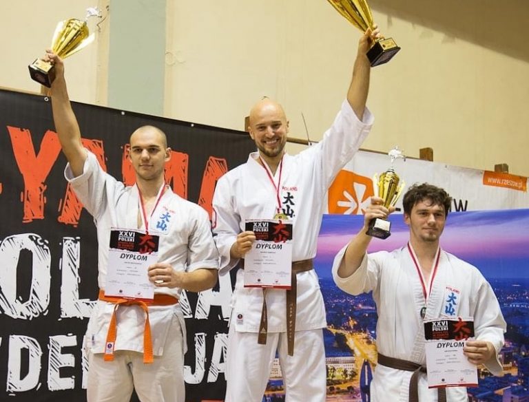 Trzej mężczyźni na sportowym podium trzymają puchary
