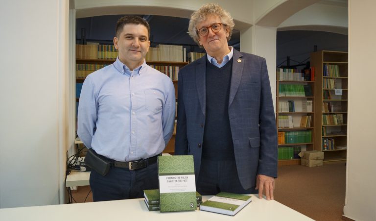 Dwaj mężczyźni stoją przed stołem, na którym leży książka