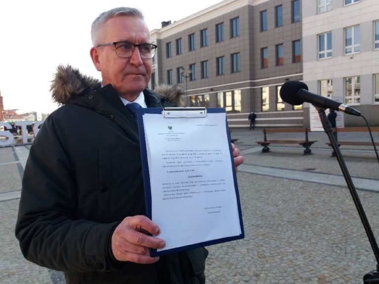 Mężczyzna stoi przed mikrofonem, w ręku trzyma papierowy dokument
