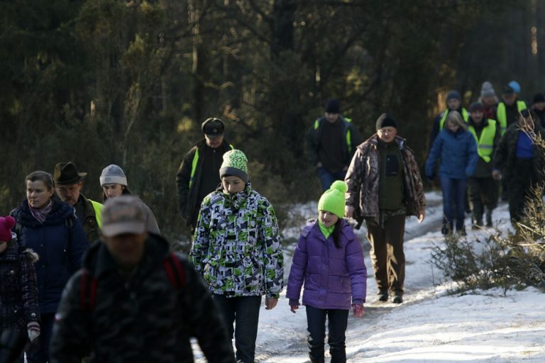 Ludzie; mężczyźni, kobiety, dzieci idą zaśnieżoną leśną ścieżką przez las