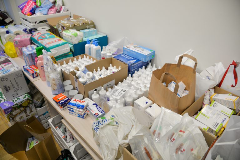 Na stole leżą zgromadzone środki medyczne; opatrunki woda utleniona, lekarstwa, środki higieniczne: maski jednorazowe, pampersy, chusteczki