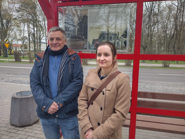 Na tle czerwonej wiaty autobusowej z przeszkleniami z lewej strony stoi mężczyzna, z prawej kobieta