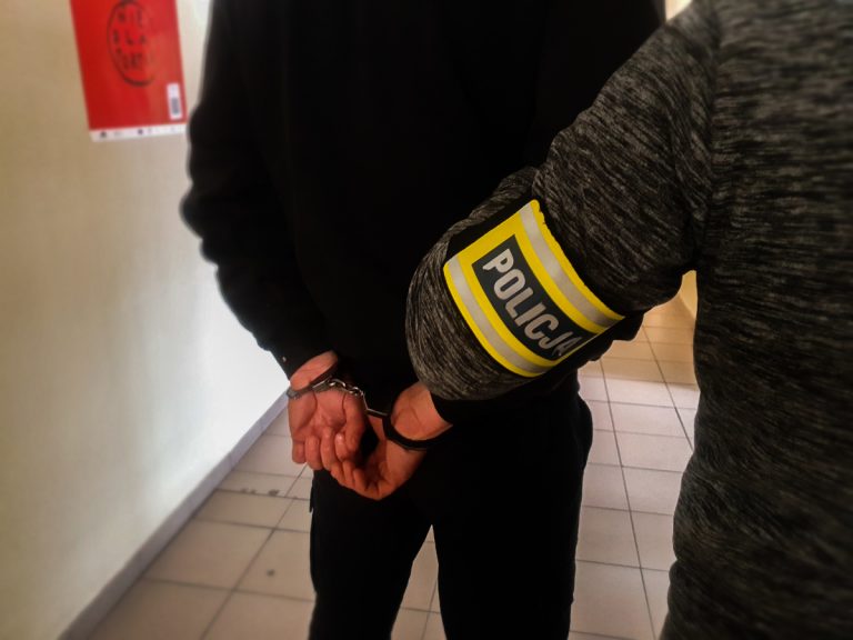 Policjant trzyma skutego kajdankami mężczyznę
