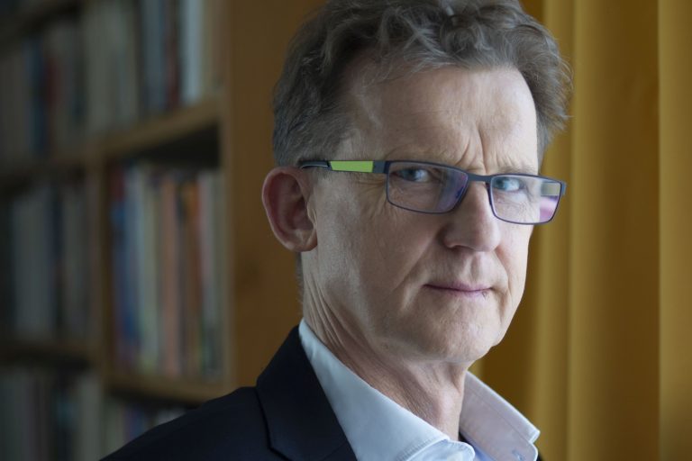 Mężczyzna w okularach na tle regału z książkami