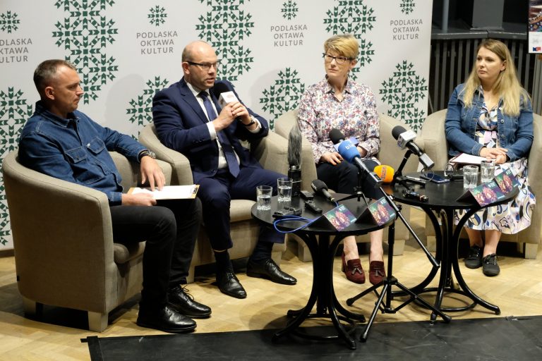Dwioe kobiety i dwóch mężczyzn siedzi przy stole przed mikrofonami