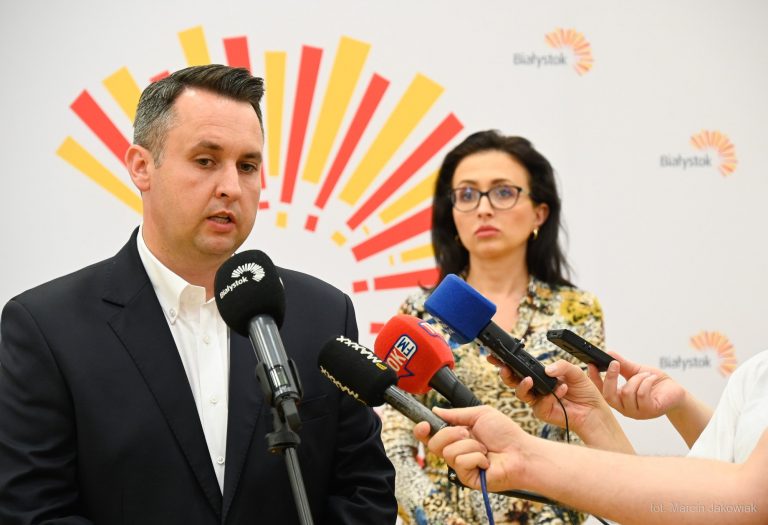 Mężczyzna mówi do mikrofonu, w tle stoi kobieta