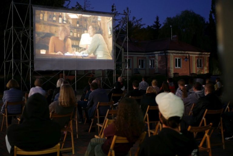 Ludzie siedzą na leżakach i oglądają film na ekranie