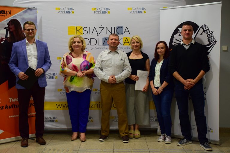 Kilka osób stoi na tle banerów promujących kampanię
