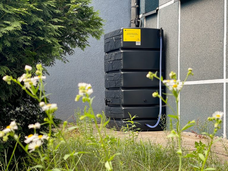 Pojemni na deszczówkę stoi przy ścianie budynku