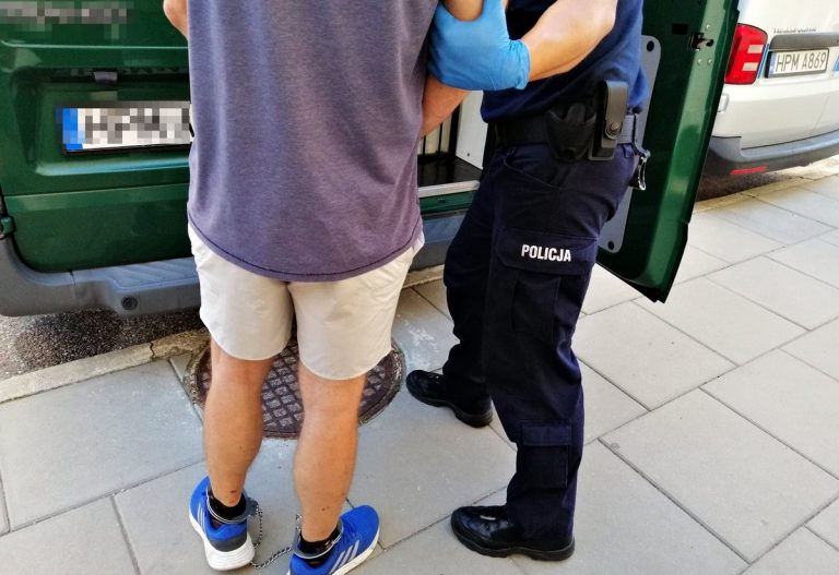 Policjant stoi przy skutym kajdankami mężczyźnie