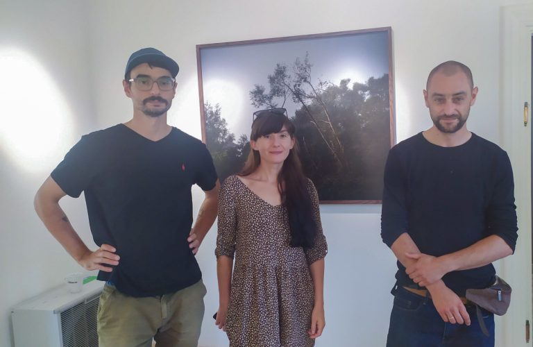dwaj mężczyźni i kobieta stoją przed fotografią wiszącą na ścianie
