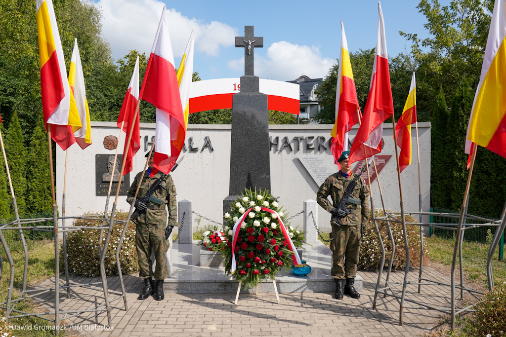 dwóch żołnierzy stoi na baczność przy pomniku, obok są flagi