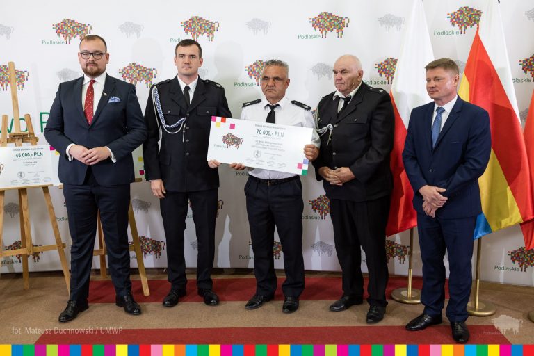 mężczyźni w garniturach, jeden z nich trzyma symboliczny czek