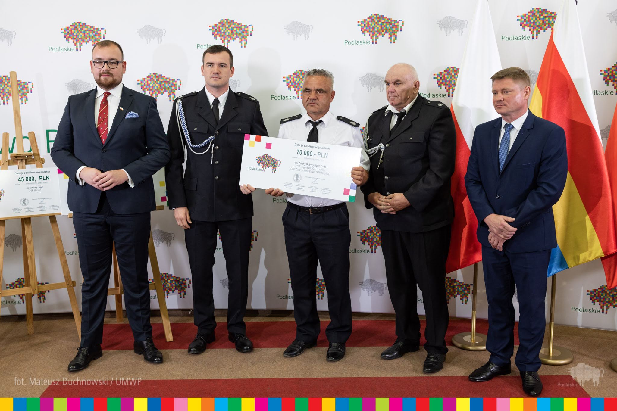 mężczyźni w garniturach, jeden z nich trzyma symboliczny czek