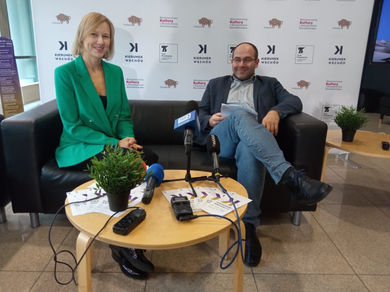 Na kanapie przy stoliku z mikrofonami siedzi kobieta i mężczyzna