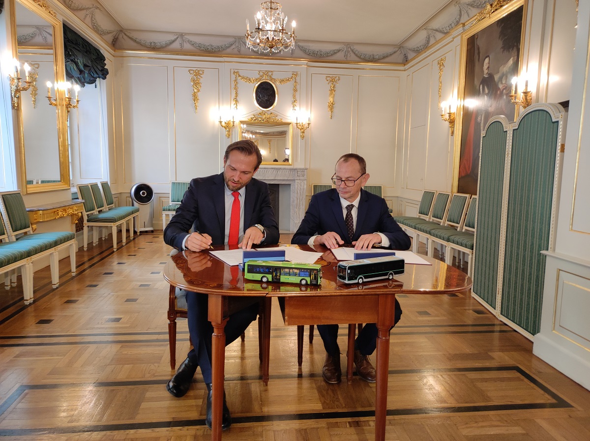 Dwaj mężczyźni siedzą przy biurku i podpisują umowę