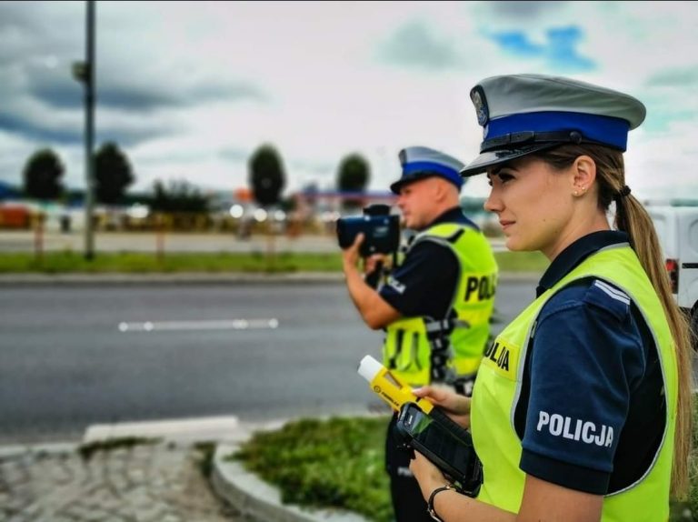 Policjant drogówki trzyma przy twarzy miernik laserowy, obok stoi policjantka trzymająca w ręku alkomat.