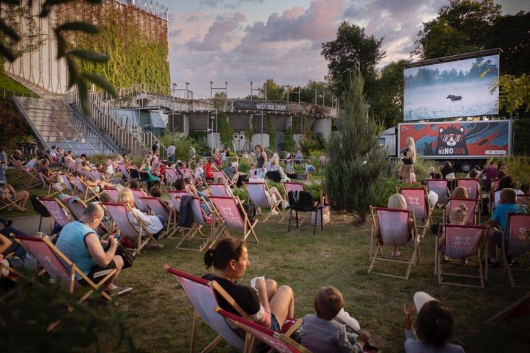 Ludzie siedzą na leżakach i oglądają film w plenerowym kinie