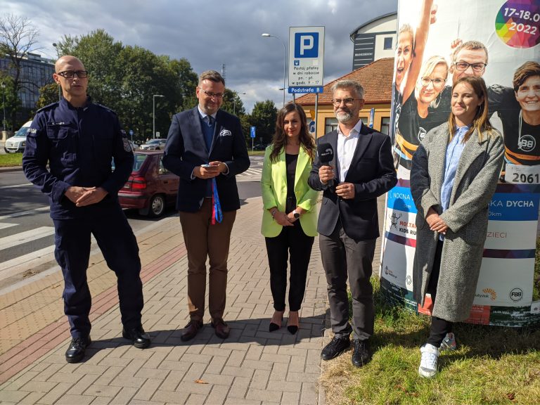 5 osób stoi na chodniku, jeden mężczyzna trzyma mikrofon
