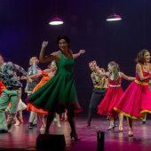 Kobiety w kolorowych sukienkach tańczą na scenie