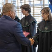 Mężzyzna w garniturze ściska dłoń uczennicy. Obok stoją inni uczniowie