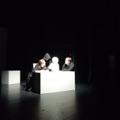 Na scenie przy białej skrzyni trzech aktorów i jedna lalka