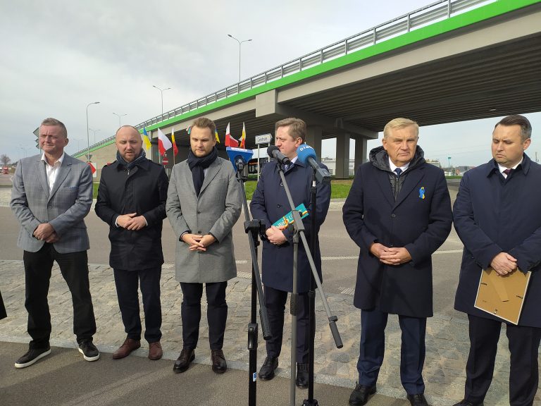Sześcioro mężczyzn stoi na chodniku przy wiadukcie obok ronda