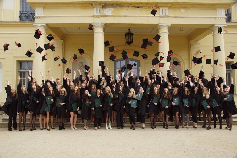 Kilkudziesięciu studentów w togach podrzuca birety