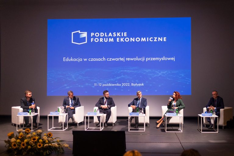 Na scenie na fotelach siedzi sześć osób, za nimi wyśietla się napis Podlaskie Forum Ekonomiczne