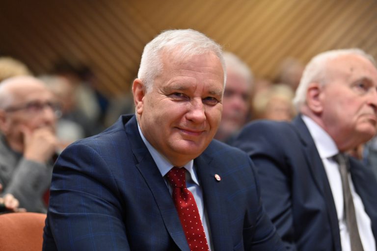 Siwy mężczyzna w garniturze uśmiecha się do obiektywu