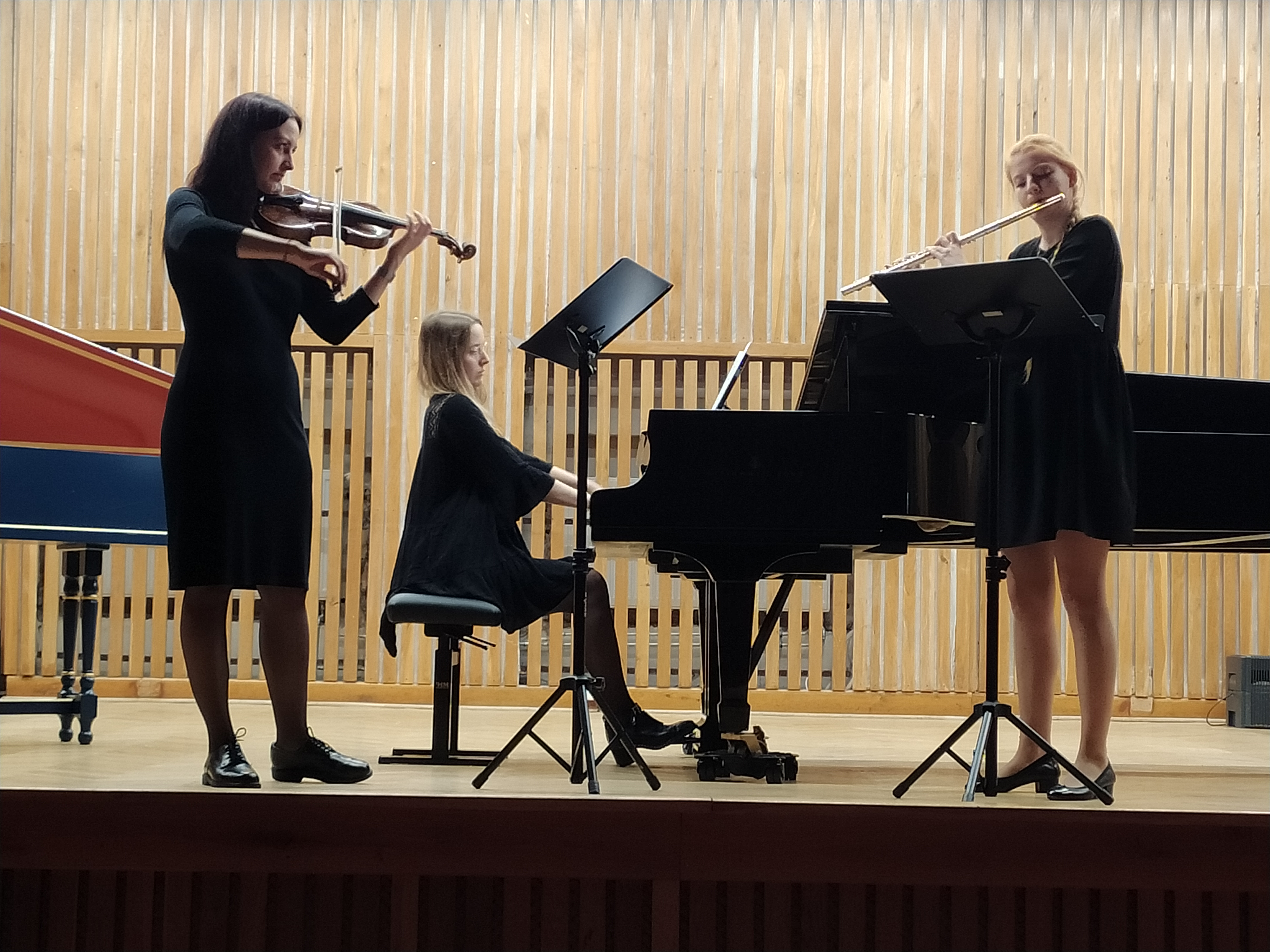 Trio muzyczne na scenie, jedna kobieta gra na skrzypcach, druga na fortepianie, a trzeba na flecie.