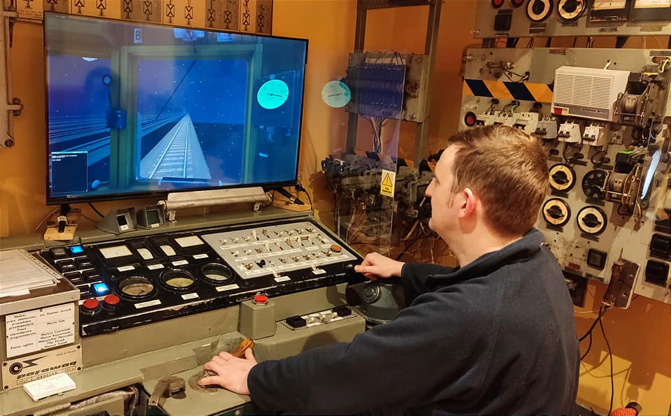 Mężczyzna siedzi przed monitorem i urządzeniami, które stanowią symulator kolejowy