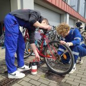 Dwóch uczniów w roboczych ubraniach naprawia rower.