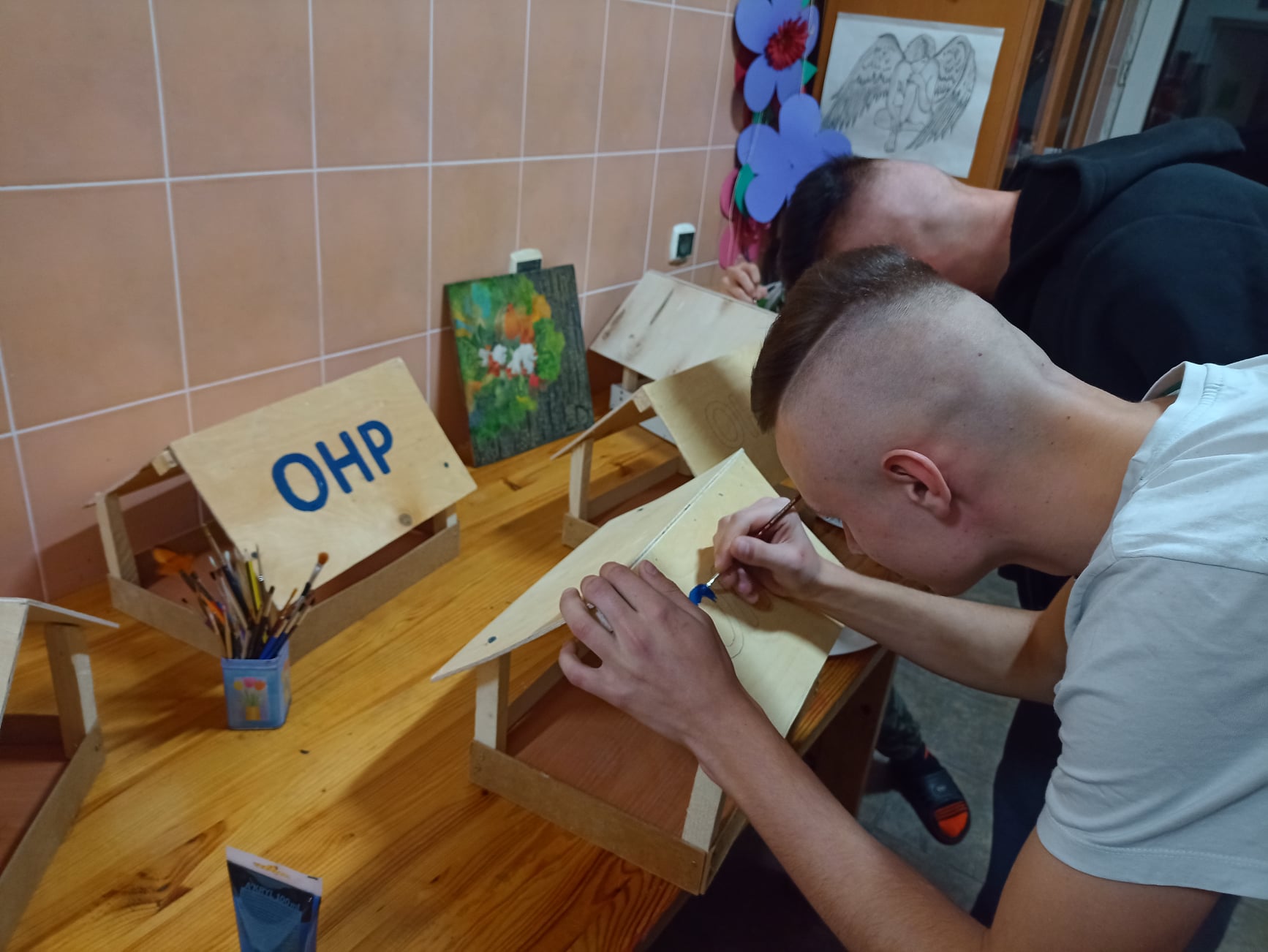 Dwóch chłopców robi karmniki dla ptaków z napisem OHP.