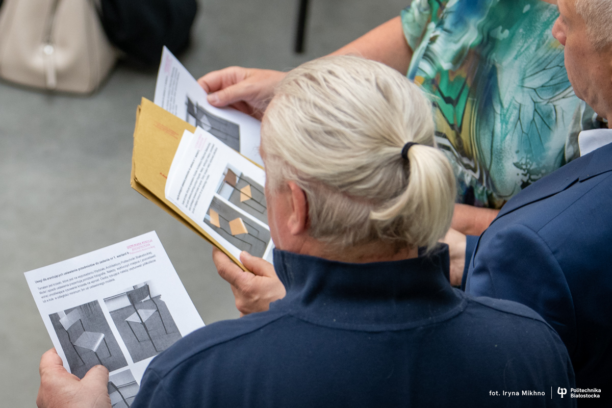 Ludzie trzymają w rękach kartki z rysunkiem krzesła.