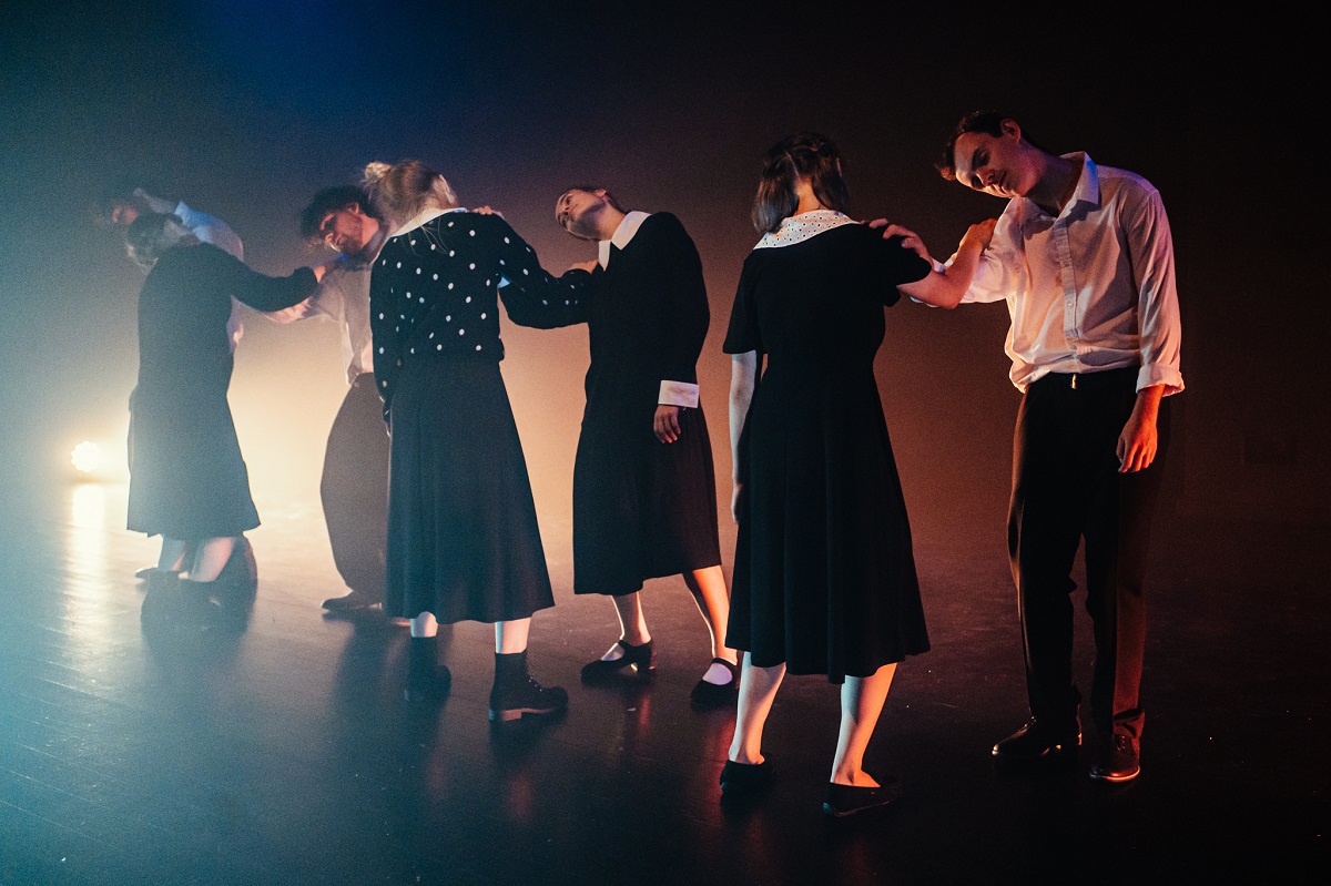 Aktorki w czarnych sukienkach tańczą na scenie.