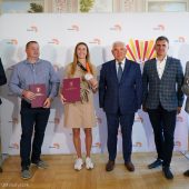Kobieta prezentuje srebrny medal obok niej stoi pięciu mężczyzn