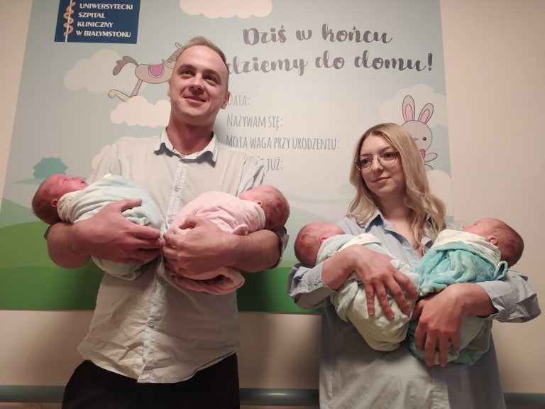 Rodzice pozują do zdjęcia trzymając na rękach czworaczki.