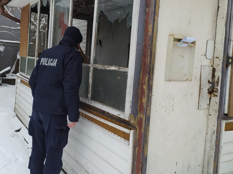 Policjant zagląda do budynku przez wybitą szybę w oknie